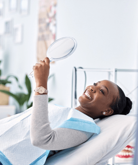 Happy dental patient holding hand mirror, admiring her smile