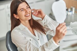 Happy dental patient admiring her smile in the mirror